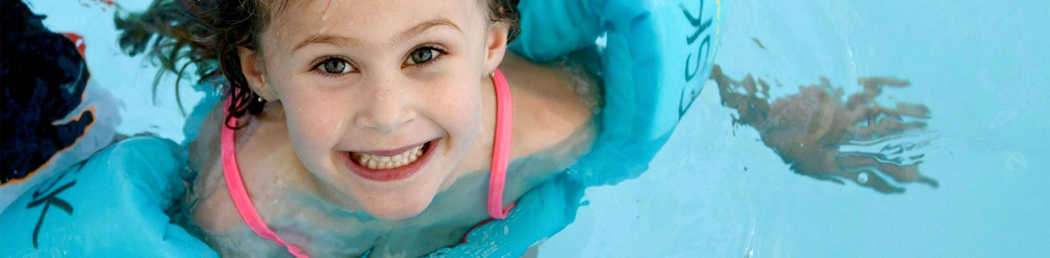 smiling girl with water wings swimming in pool