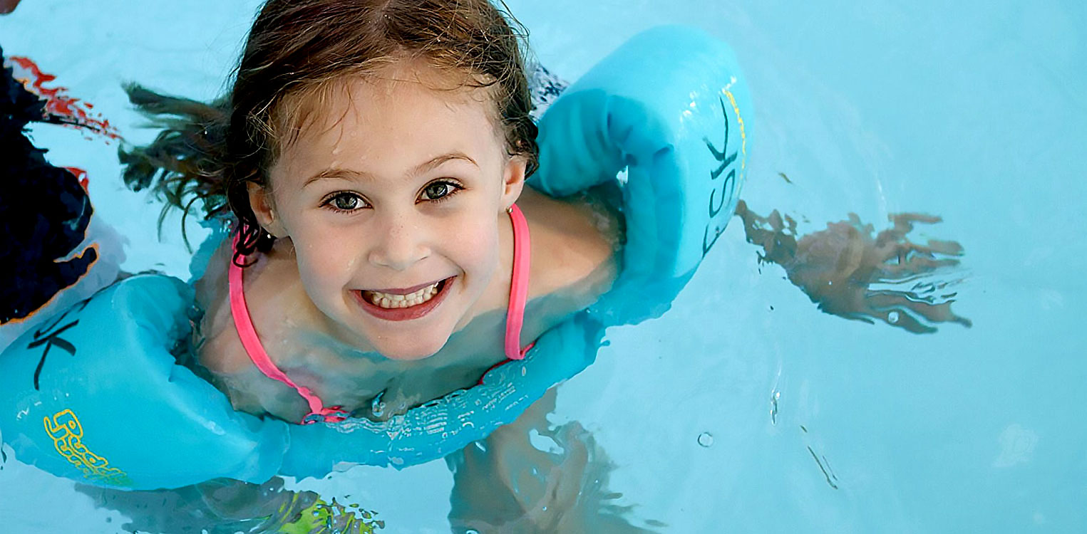 smiling girl with water wings swimming in pool